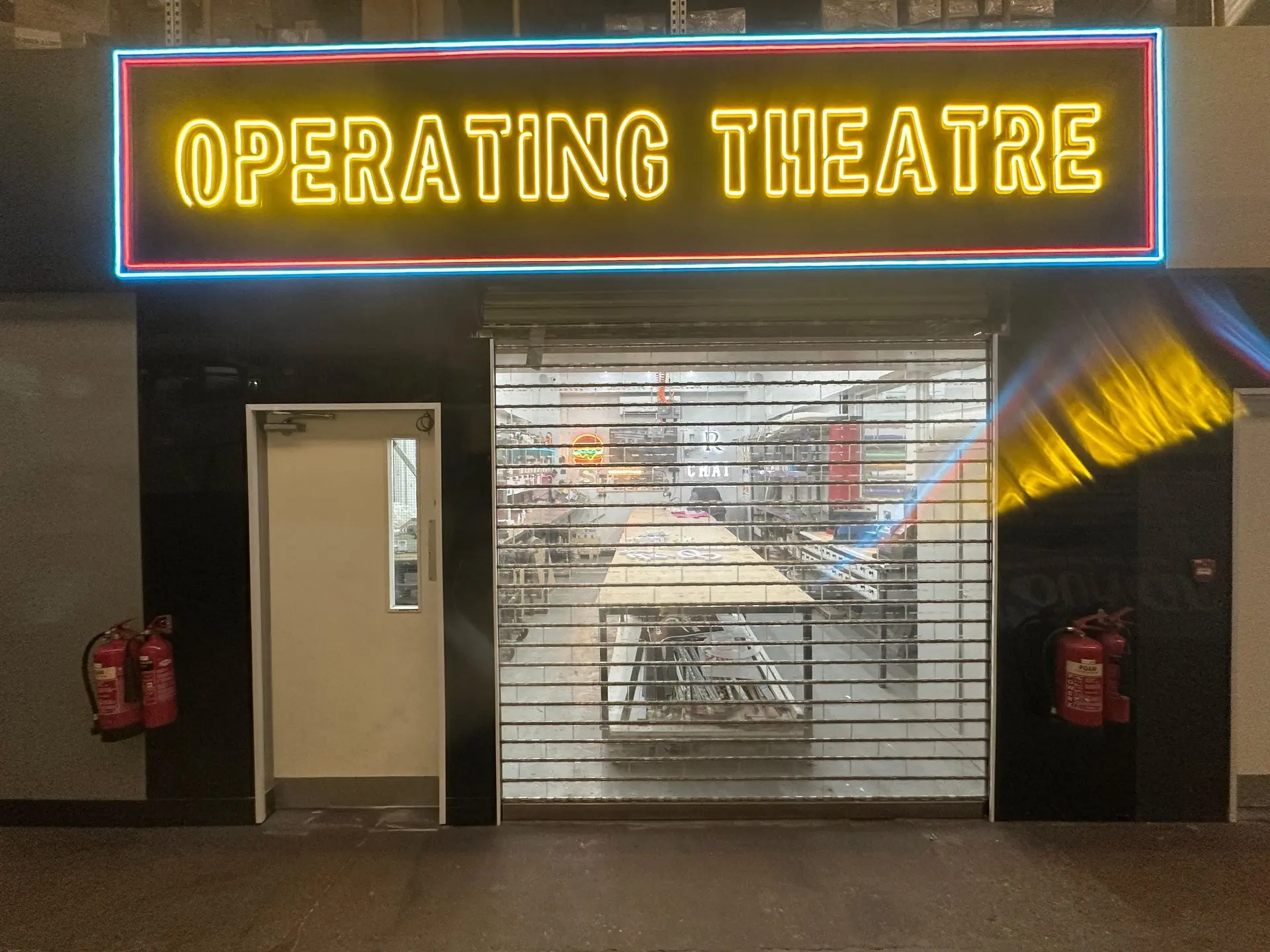 Sign Architects London workshop entrance with illuminated ‘Operating Theatre’ sign above, showcasing creative signage and fabrication space.