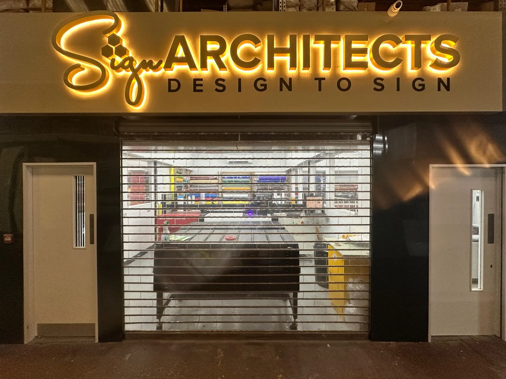 Sign Architects London showroom exterior with illuminated signage and open workshop visible, showcasing craftsmanship and design.